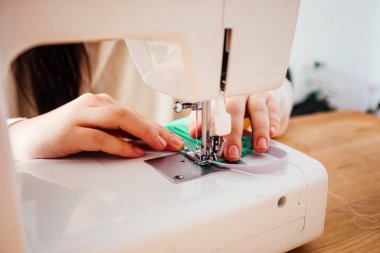 Profesyonel terzi koruyucu tıbbi maske dikiyor, yakından bakıyor.