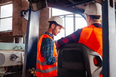 Mutlu kadın forklift sürücüsü gülümsüyor, kameraya bakıyor.