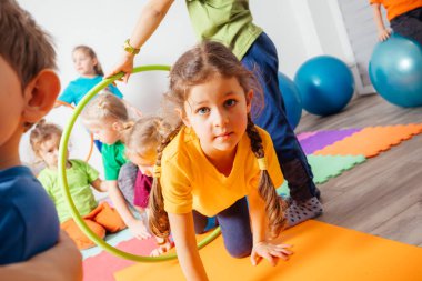 Kıvırcık kız hula çemberlerinden sürünerek geçiyor.