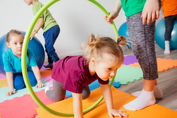 Krullend meisje kruipen op kleurrijke vloer door hula hoepels — Stockfoto