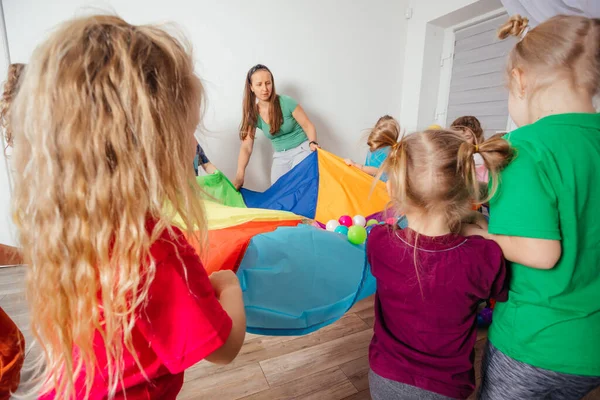Nauczyciel i przedszkolaki bawią się kolorowym spadochronem — Zdjęcie stockowe