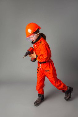 Kırmızı mühendislik üniforması giymiş küçük kız elinde bir tornavida tutuyor.