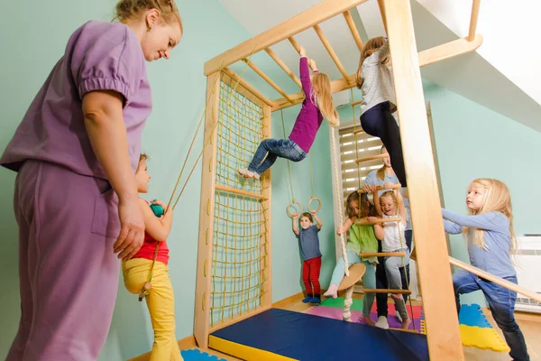 Teacher engages children to exercise on a wooden sport complex — Stock Photo, Image