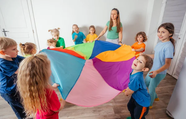 Učitel a školka děti hrát s barevným padákem — Stock fotografie
