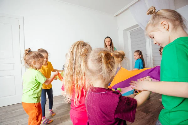 Lehrer und Kindergartenkinder spielen mit buntem Fallschirm — Stockfoto