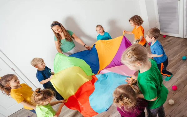 カラフルなパラシュートで遊んでいる教師と幼稚園の子供たち — ストック写真