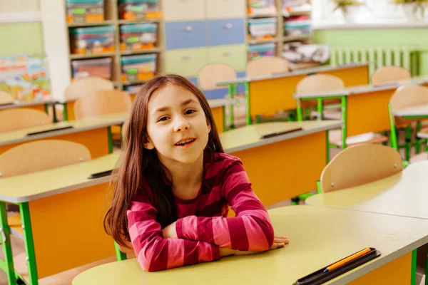 La colegiala alegre está sentada en un escritorio en el aula — Foto de Stock