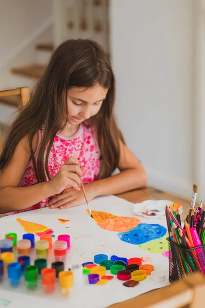 Mała dziewczynka maluje farbami sama w domu. — Zdjęcie stockowe