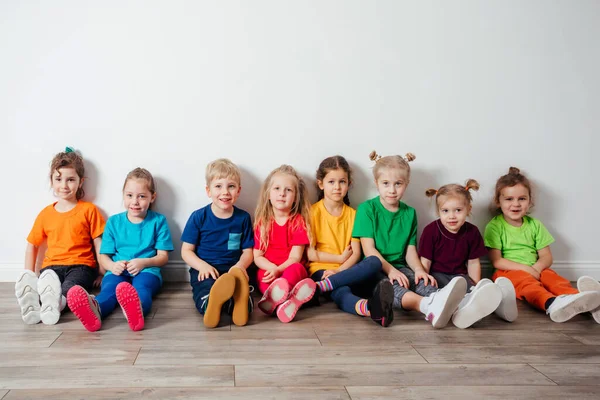 Wesołe dzieci siedzące na podłodze przy ścianie — Zdjęcie stockowe