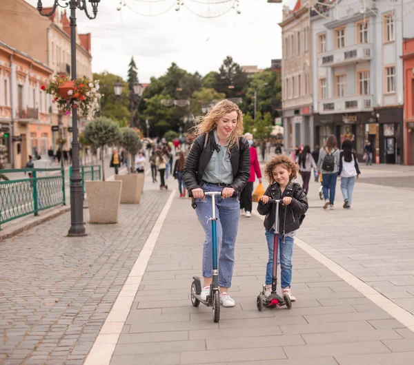 De gelukkige moeder en dochter staan met scooters in de stad — Stockfoto