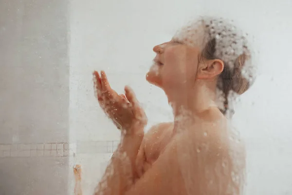 Showering woman behind glass door with water drops — Stock Photo, Image