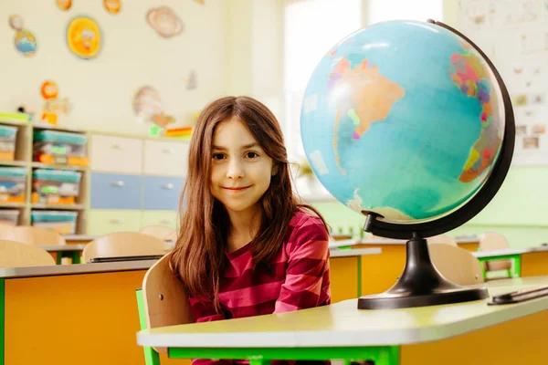 Az örömteli iskoláslány egy asztalnál ül az osztályteremben. — Stock Fotó