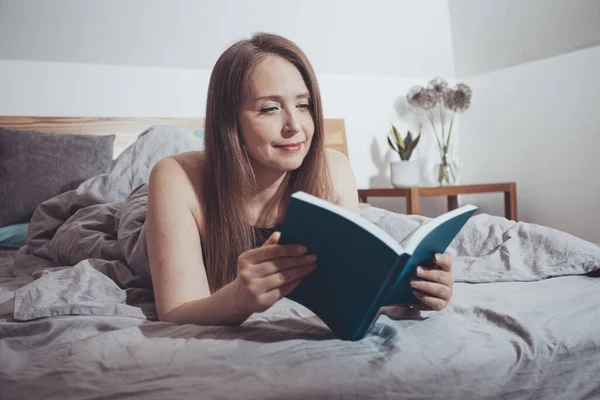 Lovely woman reading, laying on comfortable bed — Stock Photo, Image