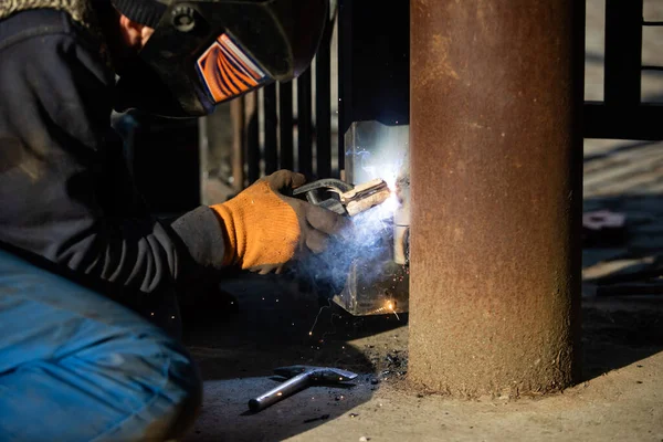 The man in uniform welds a metal at the factory