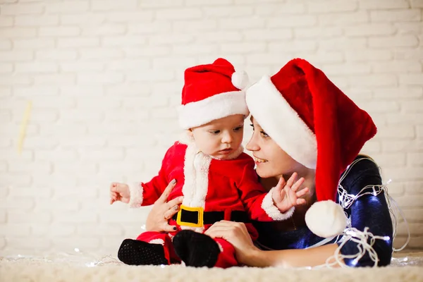 Maman avec bébé en costume de Père Noël enchevêtré dans les guirlandes — Photo