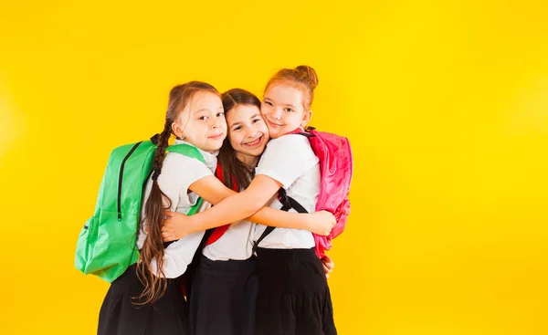 Drie meisjes klasgenoten knuffelen op een gele achtergrond — Stockfoto