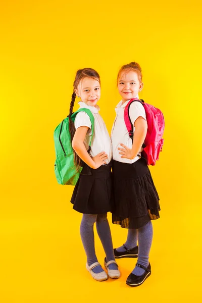 Twee vriendelijke schoolmeisjes in uniform houden hun handen aan de riem. — Stockfoto