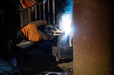 Üniformalı adam fabrikada metal kaynak yapıyor.