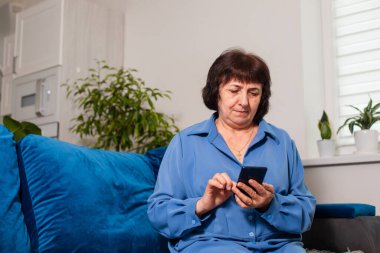 Akıllı telefondan sosyal medyada gezinen mutlu, yaşlı bir kadın.