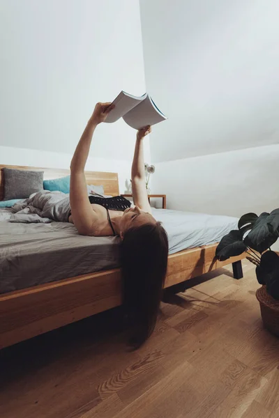 Young girl cant stop reading, lying in bed on her back — Stock Photo, Image