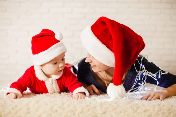 Mamma med bebis i tomtedräkt insnärjd i girlanger — Stockfoto