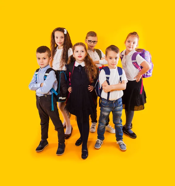 Schoolkinderen met rugzakken en gekruiste handen staande over gele achtergrond — Stockfoto