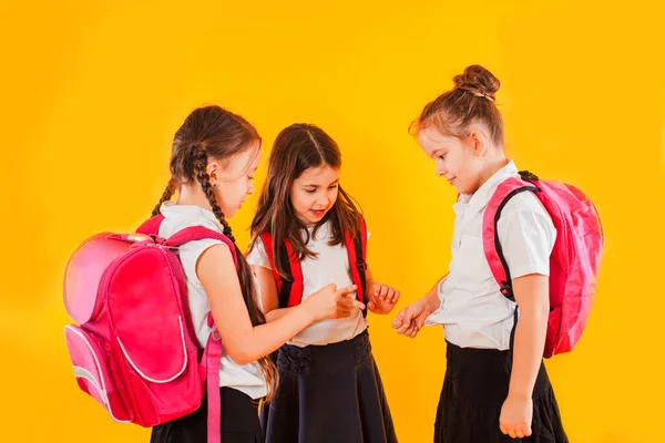 Cute girls in uniform with backpacks on yellow background — Stock Photo, Image