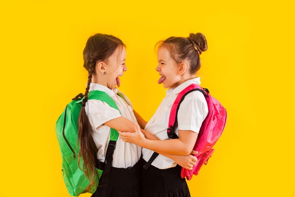 Twee lachende schoolmeisjes in uniform knuffelen naar de gele — Stockfoto