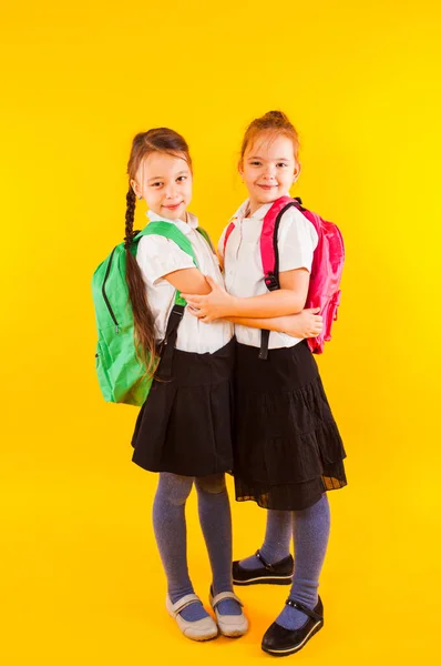 Twee meisjes klasgenoten knuffelen op een gele achtergrond — Stockfoto