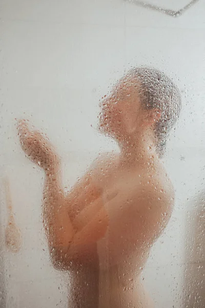 Showering woman behind glass door with water drops — Stock Photo, Image