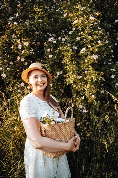 Jolie femme au chapeau tenant panier avec des fleurs — Photo