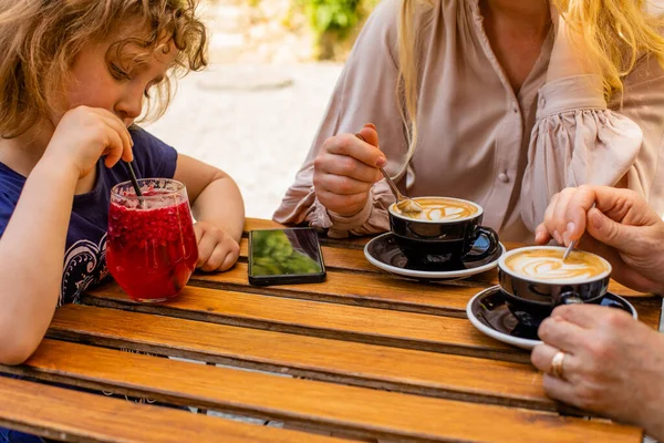 La niña con mamá y la abuela bebe jugo en un café — Foto de Stock