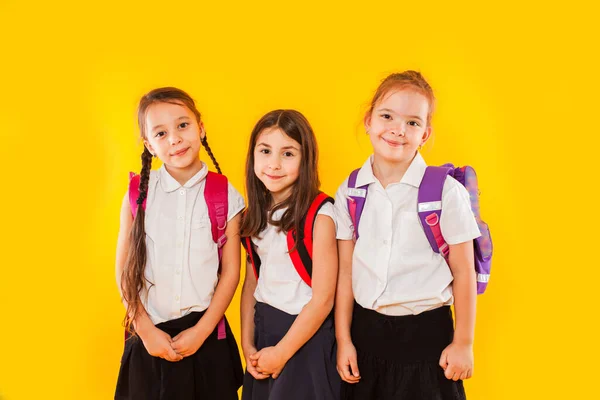 Leuke meisjes in uniform met rugzakken op gele achtergrond — Stockfoto