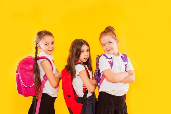 Leuke meisjes in uniform met rugzakken op gele achtergrond — Stockfoto