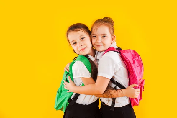 Две улыбающиеся школьницы в форме обнимаются у желтого. — стоковое фото