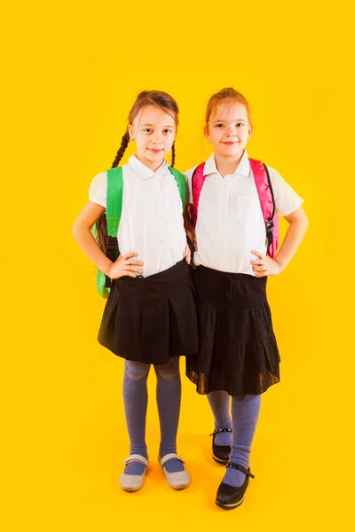 Twee vriendelijke schoolmeisjes in uniform houden hun handen aan de riem. — Stockfoto