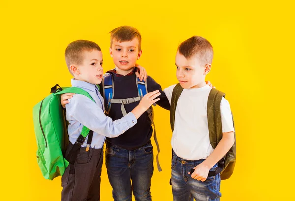 Estudantes bonitos em uniforme com mochilas no fundo amarelo — Fotografia de Stock