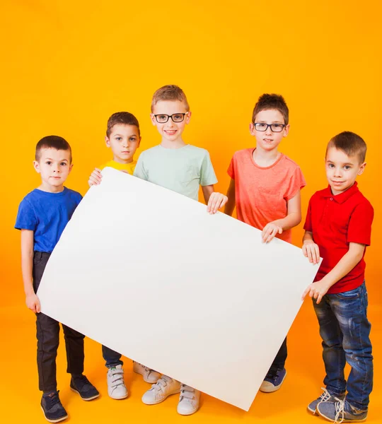 De gelukkige verschillende jongens houden een groot wit papier vast. — Stockfoto