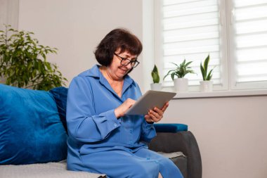 Rahatlamış olgun bir kadın elinde tablet tutarken sağlık hizmetleri uygulaması kullanıyor.