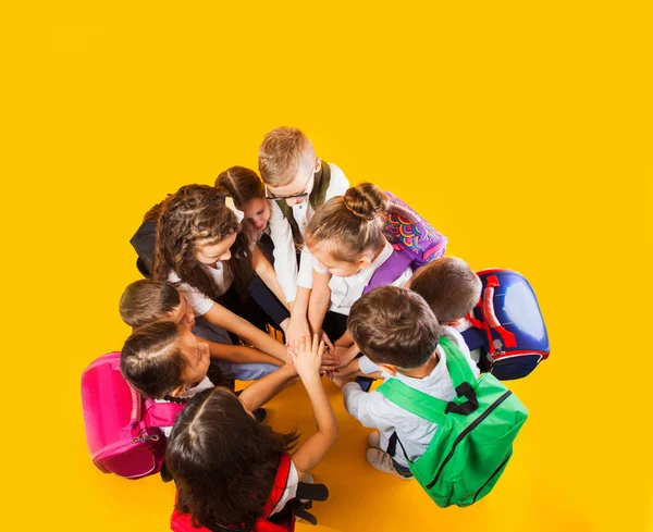 Az iskolások egymásra rakják a kezüket a sárga háttérben. — Stock Fotó