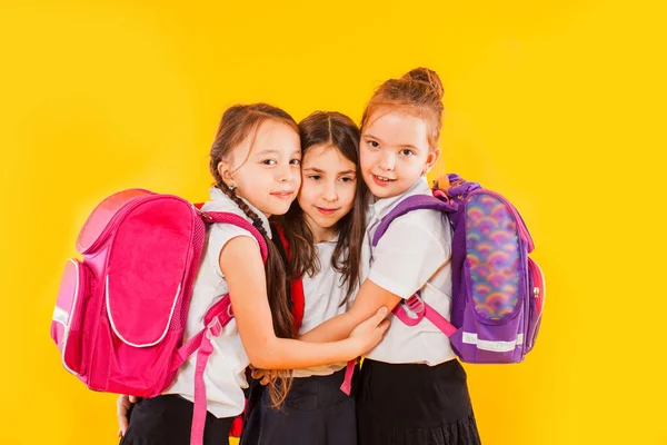 Leuke meisjes in uniform met rugzakken op gele achtergrond — Stockfoto