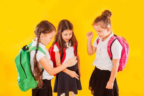 Chicas lindas en uniforme con mochilas sobre fondo amarillo —  Fotos de Stock