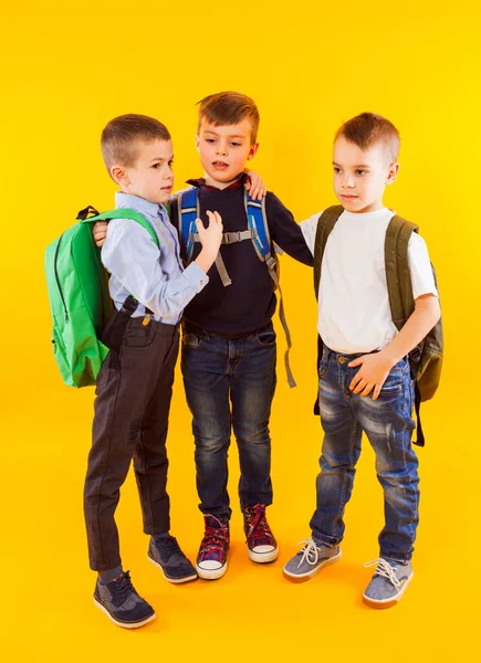 Lindos colegiales en uniforme con mochilas sobre fondo amarillo —  Fotos de Stock