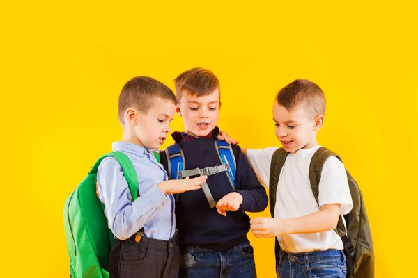 Écoliers mignons en uniforme avec des sacs à dos sur fond jaune — Photo