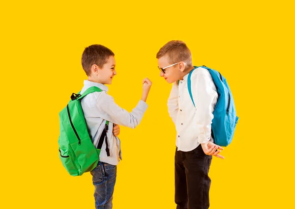 Lindos colegiales en uniforme con mochilas sobre fondo amarillo —  Fotos de Stock