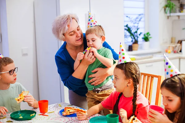 Supportive mother helping little boy to blow party horn — Stock Photo, Image
