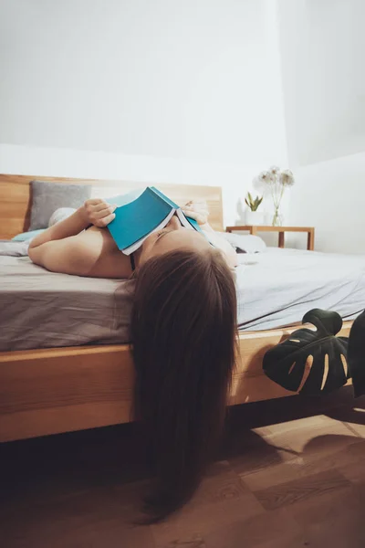 女の子は読書を止めることができない、彼女の背中にベッドに横たわって — ストック写真