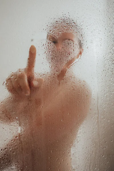 Cheerful woman drawing heart on condensed glass door — Stock Photo, Image