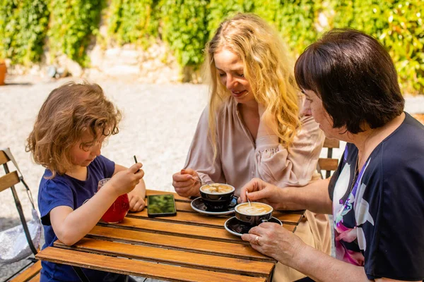 The little girl with mom and grandma drinks juice in a cafe — Stock Photo, Image