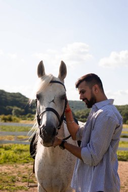 Mutlu adam çiftlikte beyaz bir atı okşuyor.